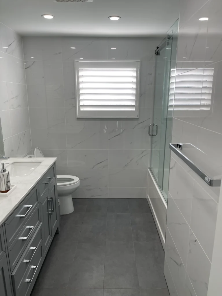 photo of modern bathroom with gray vanity toilet glass shower and white marble look wall tiles