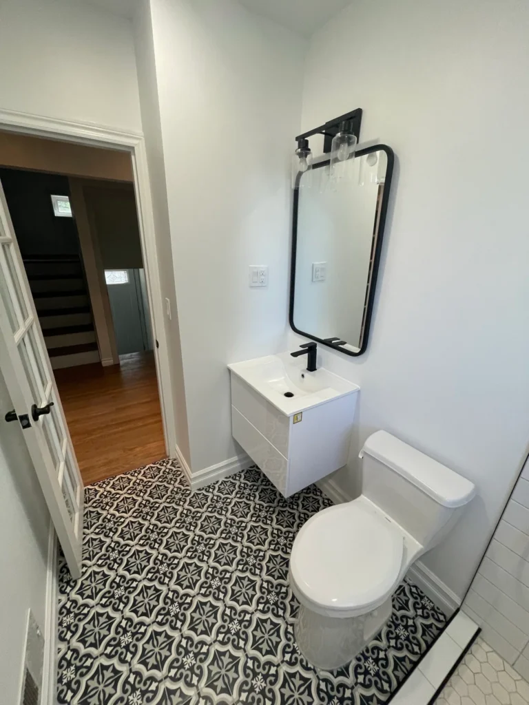 photo of modern small bathroom with patterned tile floor wall mounted sink toilet and mirror showing what is a powder room layout