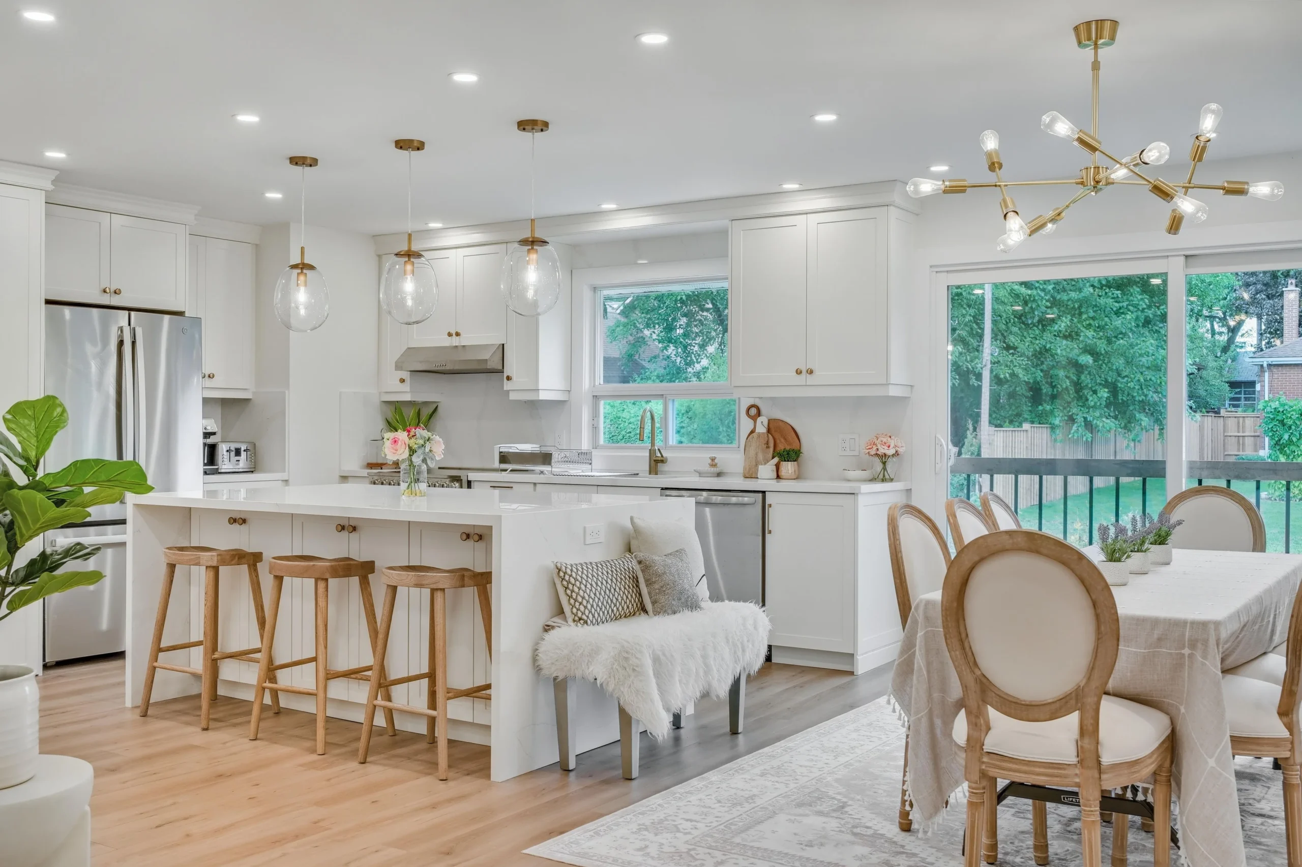 photo bright open kitchen and dining area with white cabinets island seating pendant lights wood flooring and large windows