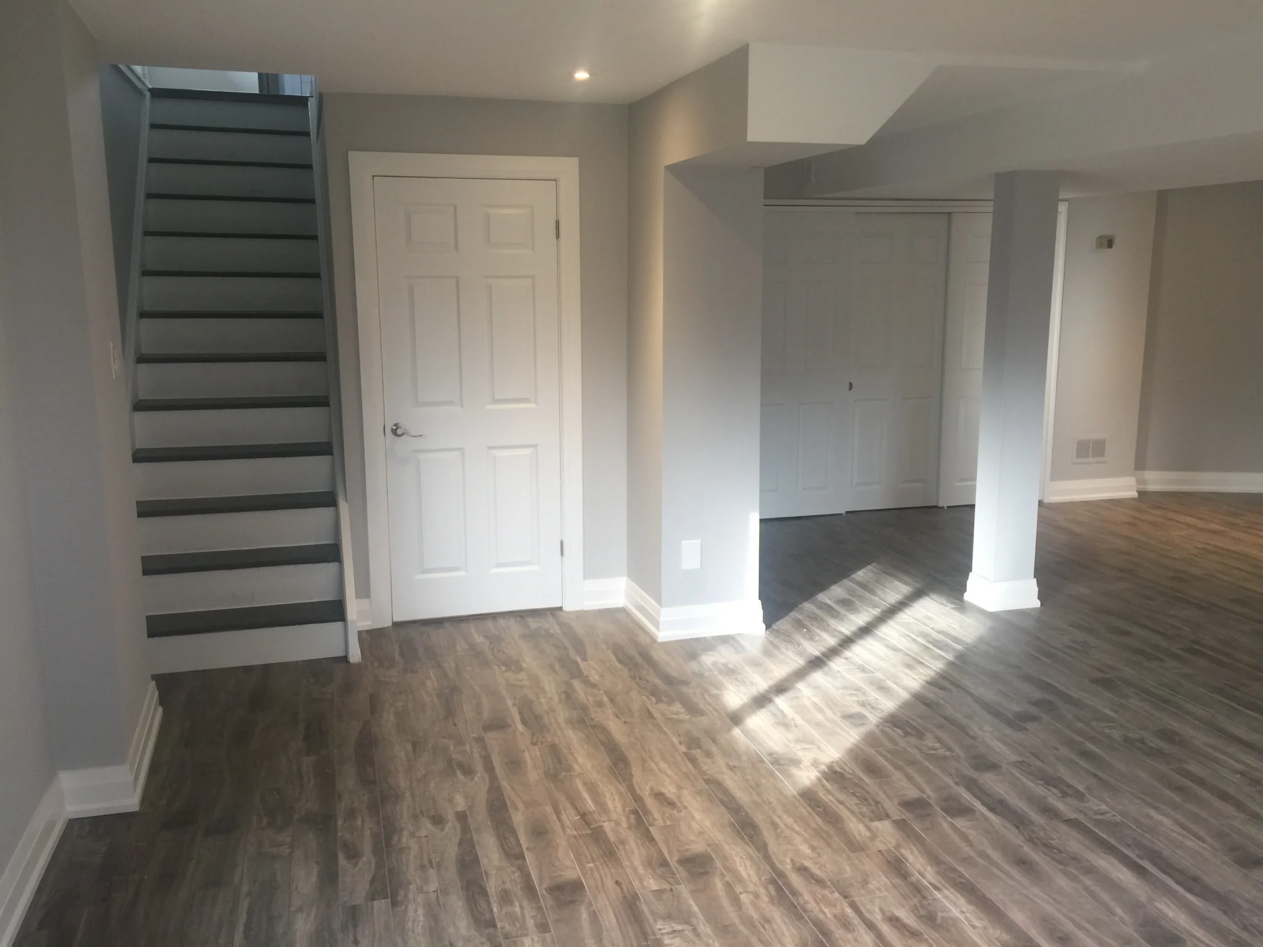 photo finished basement with stairs white door support column open space and wood flooring