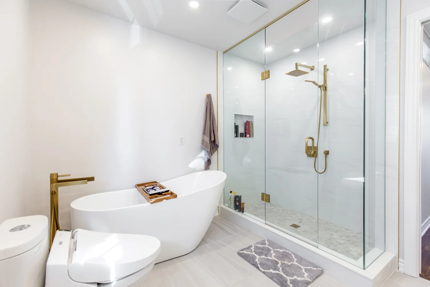 photo-of-modern-bathroom-with-freestanding-tub-glass-shower-gold-fixtures-white-walls-toilet-and-gray-floor-mat