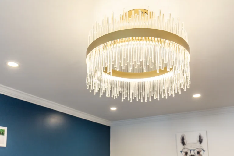 photo-of-modern-gold-chandelier-with-hanging-crystal-rods-on-white-ceiling-with-recessed-lights-and-blue-accent-wall