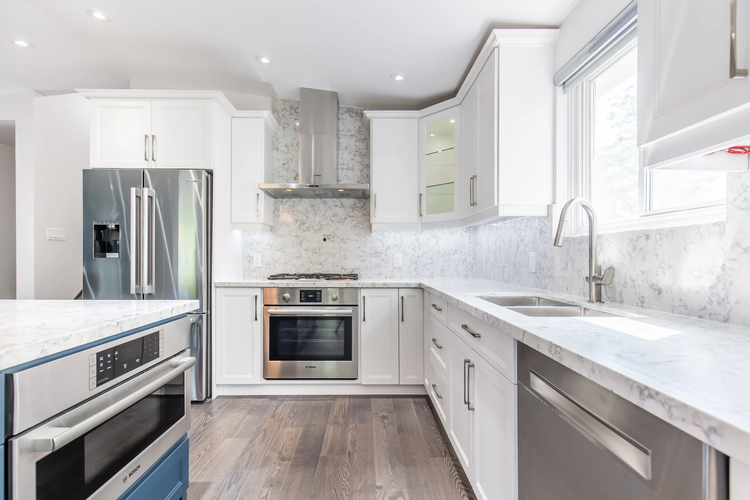 photo home renovations stoney creek modern white kitchen with marble countertops stainless steel appliances built in oven range hood recessed lighting wood flooring and large window