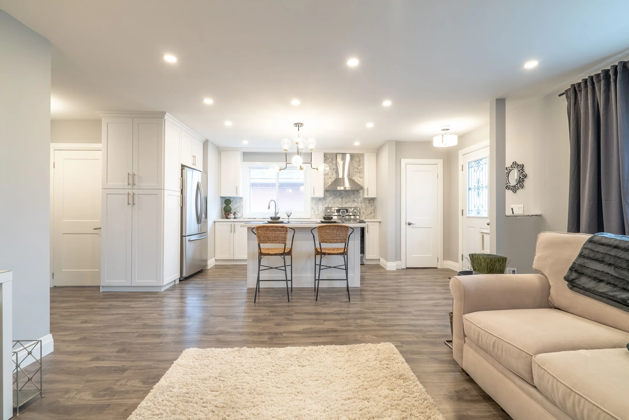 photo open concept living and kitchen space with island stools pendant lighting white cabinets sofa area rug and wide plank flooring