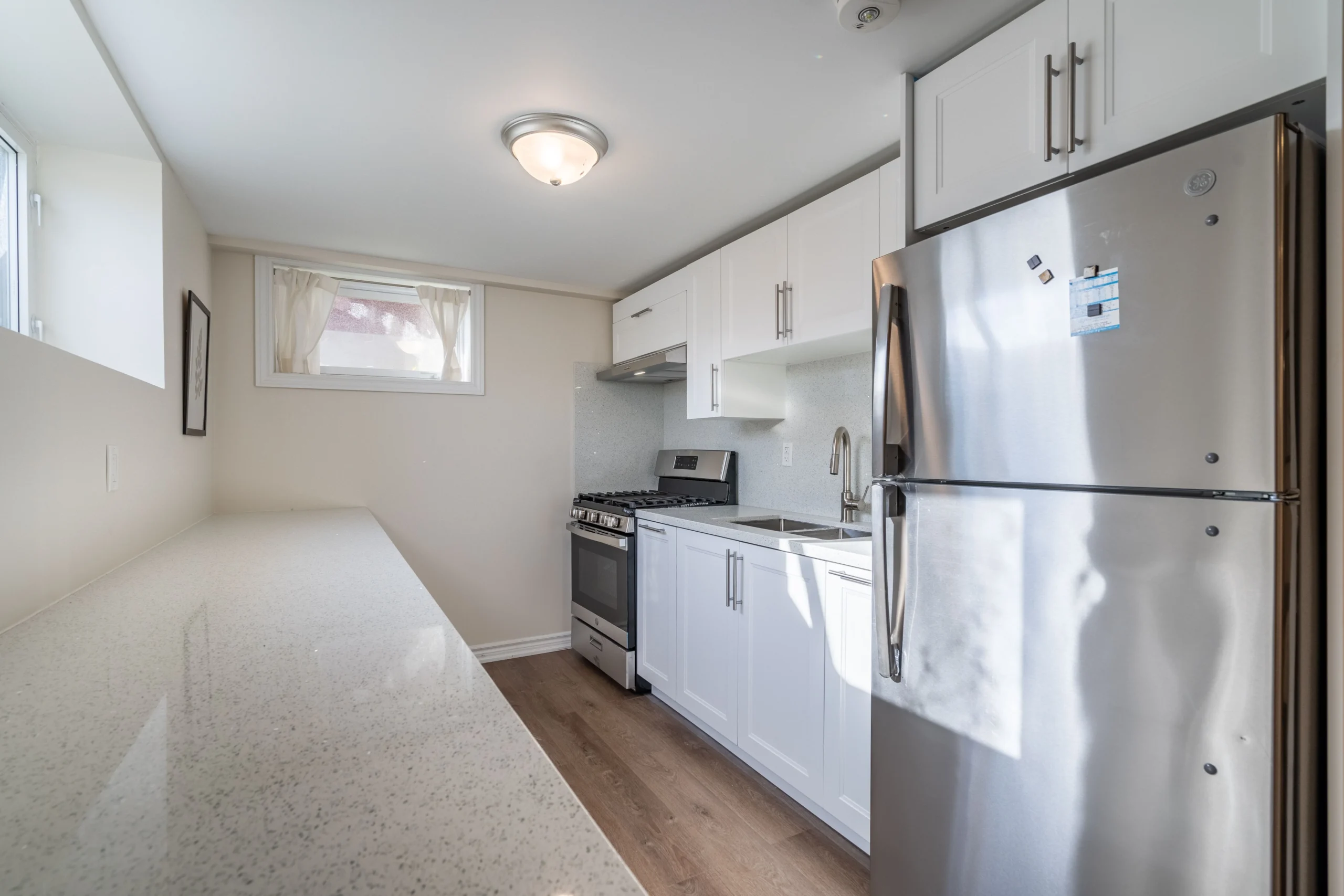 photo-small-kitchen-with-white-cabinets-stainless-steel-fridge-stove-sink-and-long-countertop-with-window-and-curtains-above