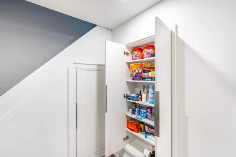 Photo open pantry cabinet stocked with household supplies under stairs