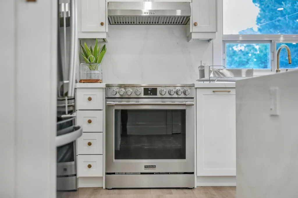 Photo stainless steel range beneath white kitchen cabinetry